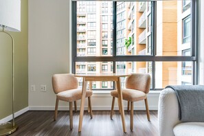 Ein Zimmer mit großem Fenster, zwei Stühlen, einem kleinen Tisch und einer Stehlampe.