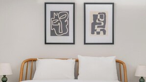 A bed with white bedding, two framed abstract artworks above it, and two bedside lamps on either side. - Blueground | Ballston, pool, nr Arlington Park (Arlington)
