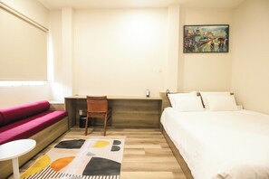 Ein Hotelzimmer mit einem Bett, einem Schreibtisch, einem Stuhl, einem kleinen Tisch, einer Couch und einem Bild an der Wand.