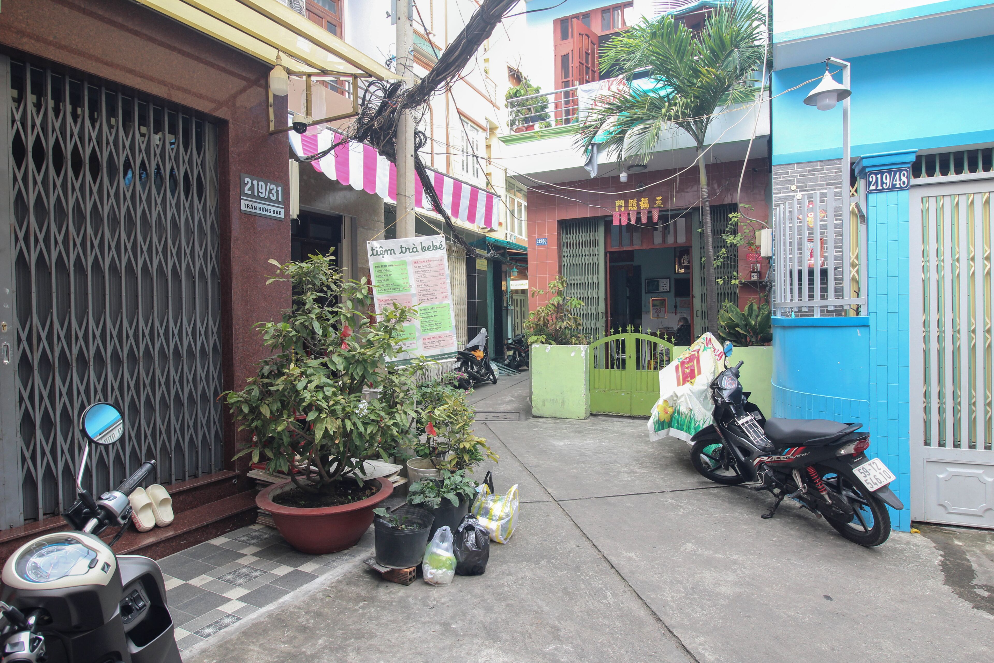 A narrow street with buildings on either side, a motorcycle parked on the right, and a potted plant in the center.