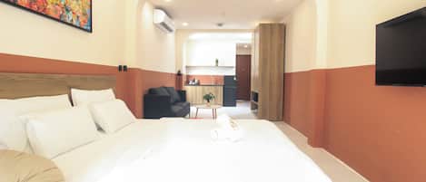 Ein Hotelzimmer mit einem großen Bett, einem an der Wand montierten Fernseher und Blick in den Küchenbereich.