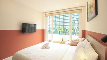 A hotel room with a bed, a television mounted on the wall, and a window with a view of buildings and greenery.