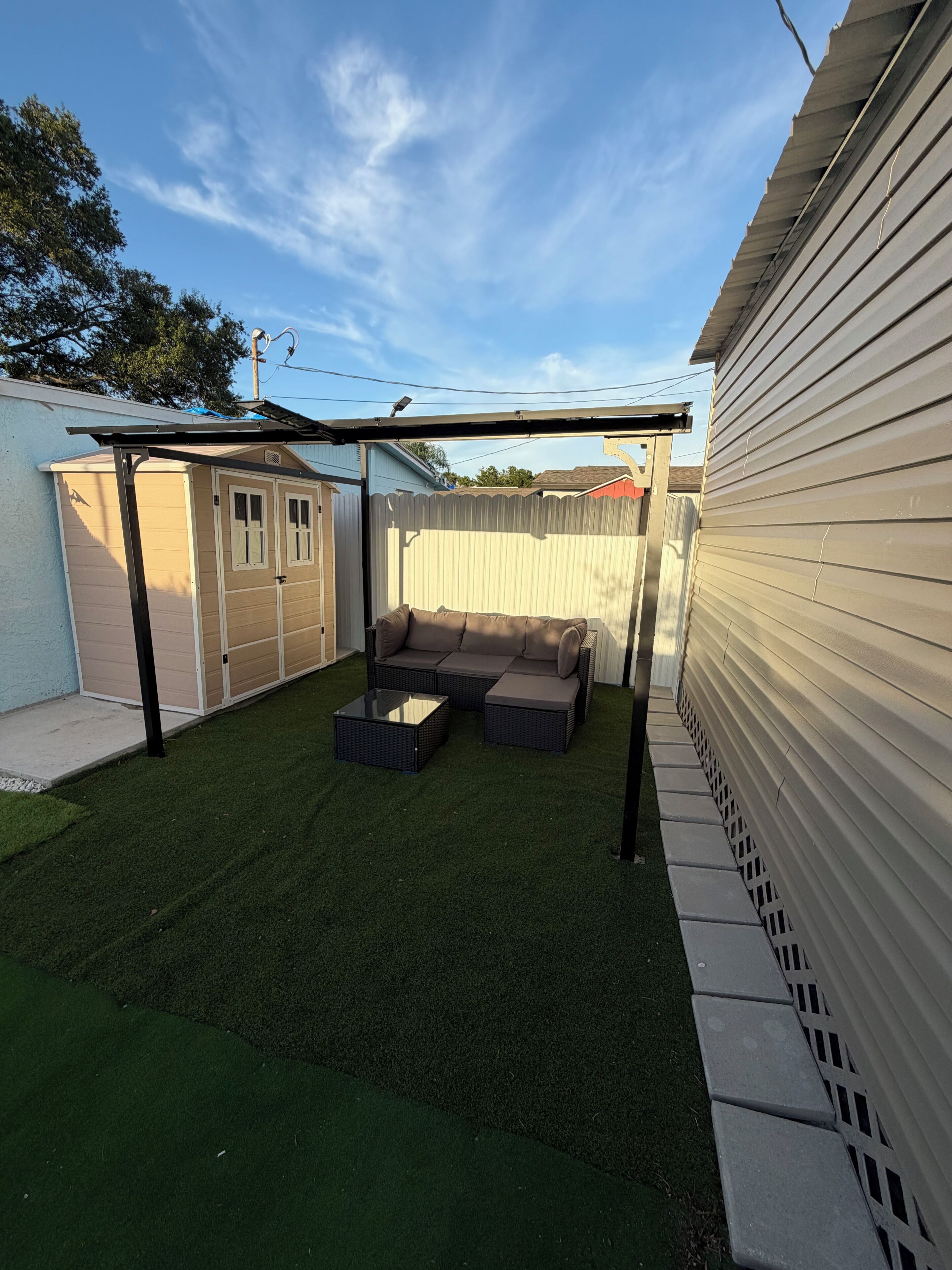 Un patio trasero con césped artificial, una zona de patio y un área de estar cubierta.