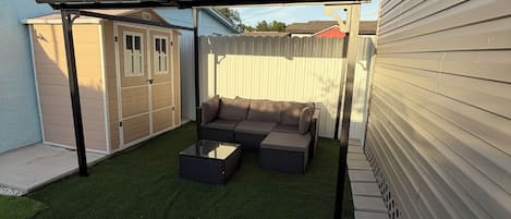 Un patio trasero con césped artificial, una zona de patio y un área de estar cubierta.
