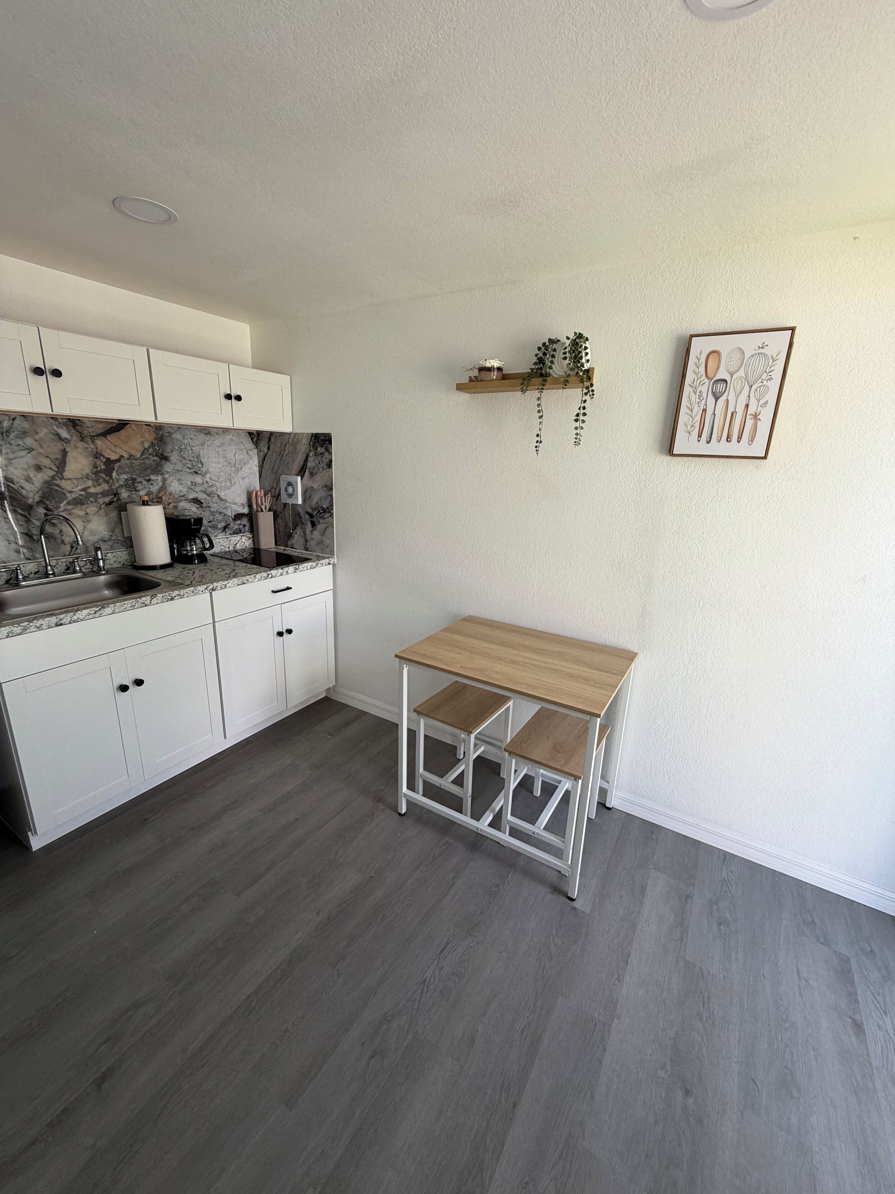 A kitchen with white cabinets, a marble backsplash, and a wooden table.