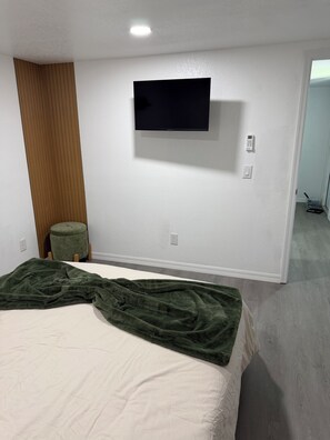 Una camera da letto con un letto, una coperta verde, una televisione a parete e un pannello di legno a sinistra.