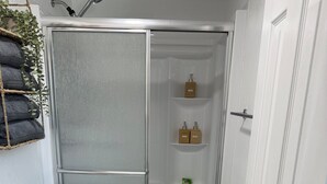 Casa de banho com sanita branca, cabine de duche envidraçada e um pequeno armário com produtos de higiene pessoal.