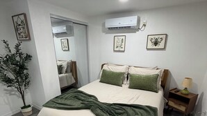 Quarto com cama, mesa de cabeceira, abajur e planta em vaso.