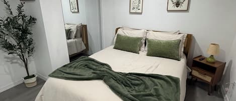 A bedroom with a bed, a bedside table, a lamp, and a potted plant.