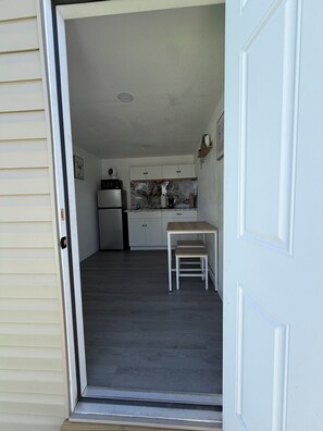 A kitchen with white cabinets, a refrigerator, a coffee maker, and a small table with a bench. - Cozy Boho Retreat (Tampa)