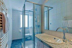 A modern bathroom with a glass shower enclosure, a sink with a mirror, and a toilet visible in the background. - Hotel Peterhof (Dietenheim)