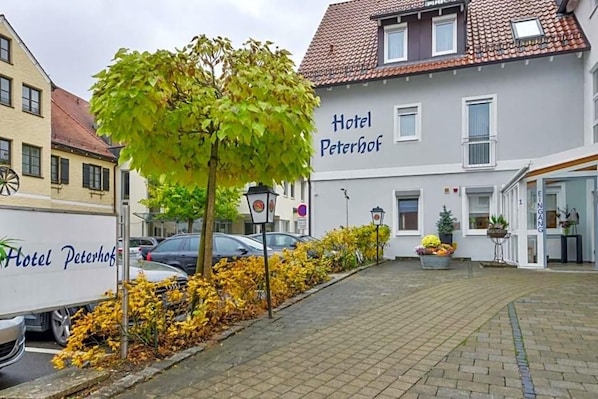 A hotel named 'Hotel Peterhof' with a paved courtyard, parked cars, and a tree. - Hotel Peterhof (Dietenheim)