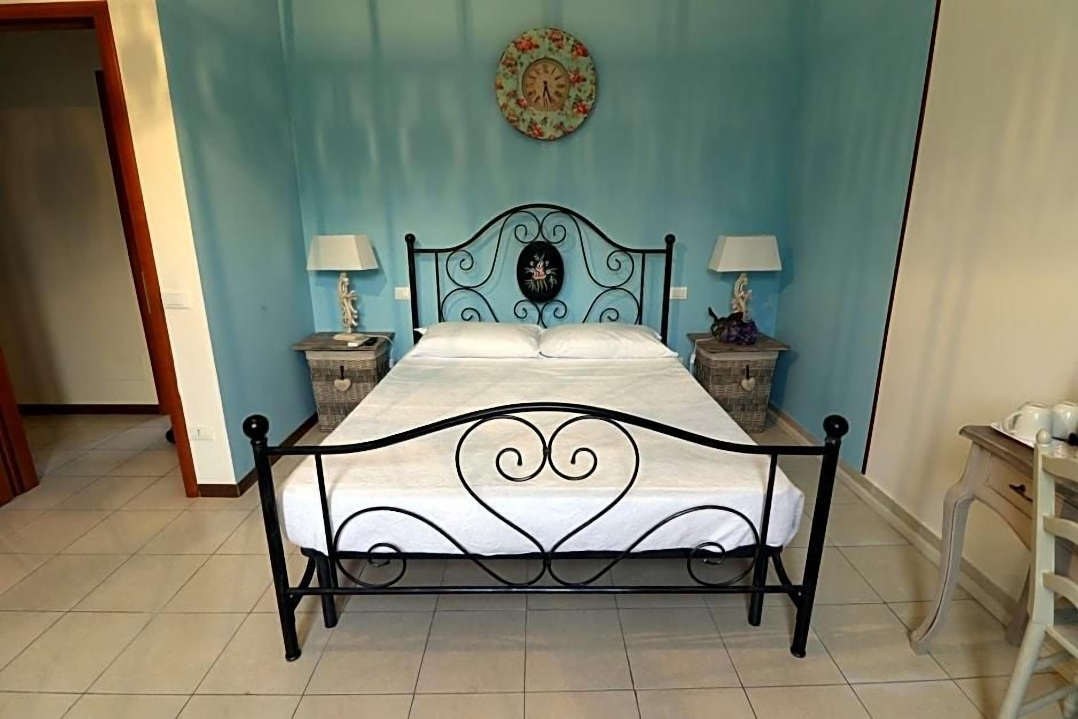 A bed with a metal frame and white bedding, two bedside tables with lamps, and a wall clock.