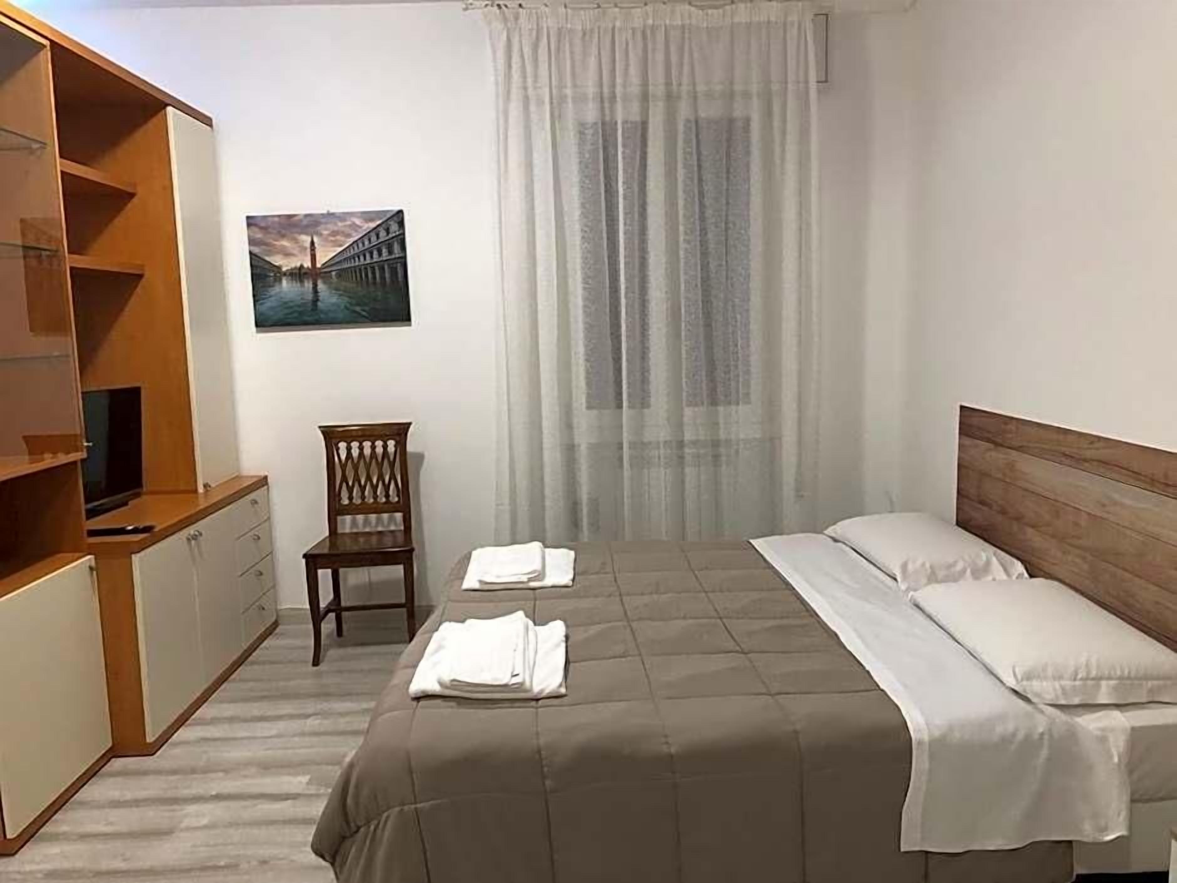 A hotel room with a bed, a chair, a TV, and a painting on the wall.