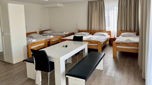 Una habitación de hotel con cuatro camas individuales, una mesa blanca con bancos y un armario.