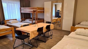 Una habitación de hotel con literas, una mesa de comedor con sillas, un espejo y un armario.