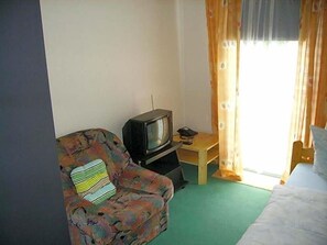 A room with a single bed, a chair with a patterned cushion, a small table, and a television. - Hotel Kraichgauidylle (Malsch)