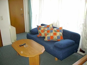 A blue sofa with colorful pillows, a wooden coffee table, and a door in the background. - Hotel Kraichgauidylle (Malsch)