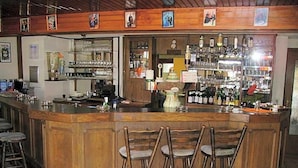 A bar area with a wooden counter, bar stools, and shelves stocked with bottles and glasses. - Hotel Kraichgauidylle (Malsch)