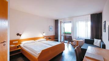 Ein Hotelzimmer mit Bett, Nachttisch, Lampe, Sofa und einem kleinen Tisch mit Stuhl.