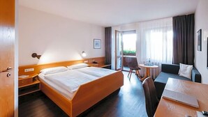 A hotel room with a bed, bedside table, lamp, sofa, and a small table with a chair. - Restaurant Landhotel Winter (Gomadingen)