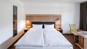 Ein Hotelzimmer mit einem großen Bett, einem Holz-Kopfteil, Nachttischlampen, einem Schreibtisch und einem Stuhl.