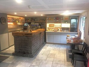Een bar met een stenen toonbank, flessen op de planken, en een zithoek met stoelen.