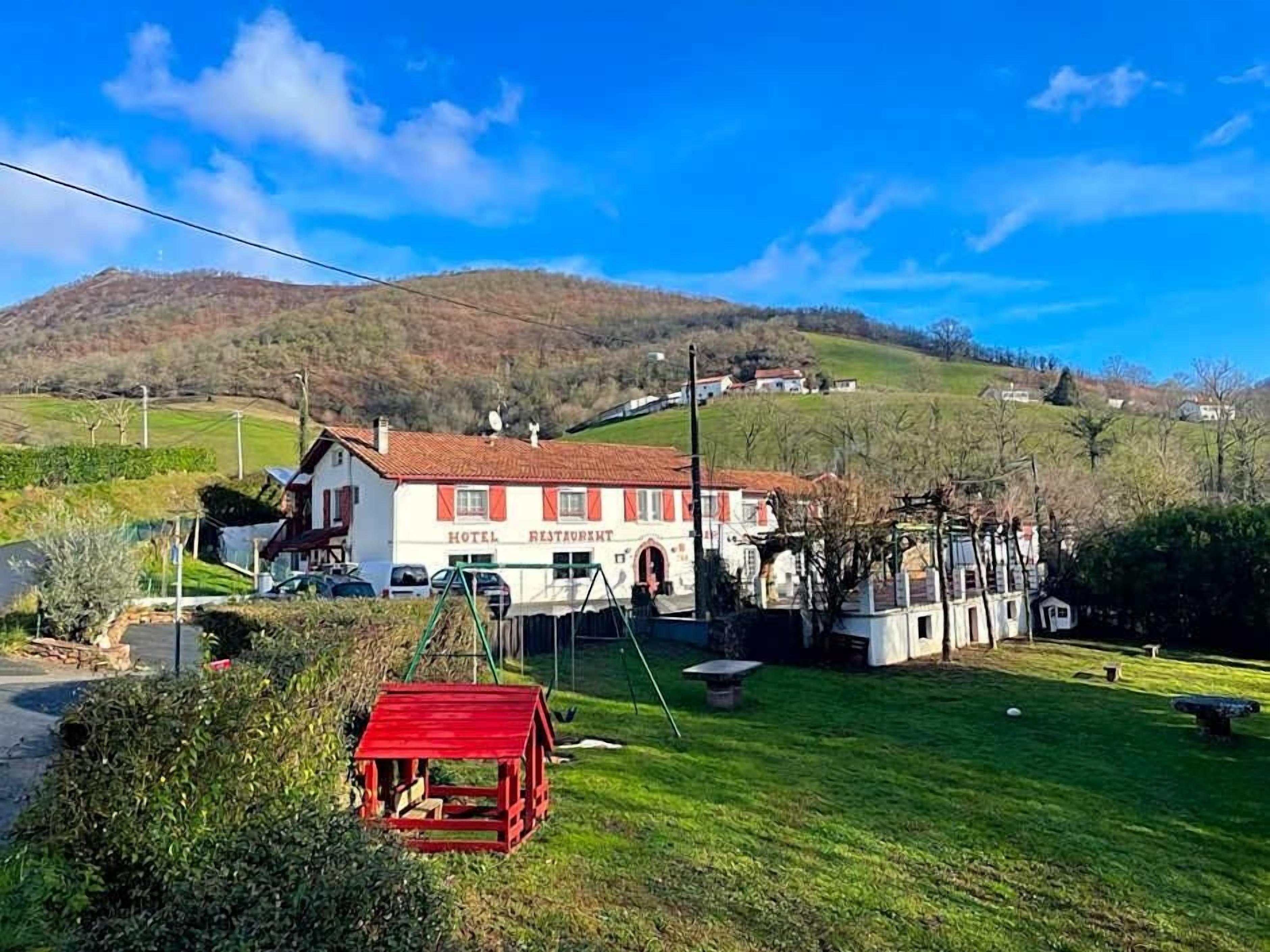 A hotel with a red-roofed building, a well-maintained lawn, and a hilly backdrop.