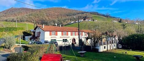 A hotel with a red-roofed building, a well-maintained lawn, and a hilly backdrop.