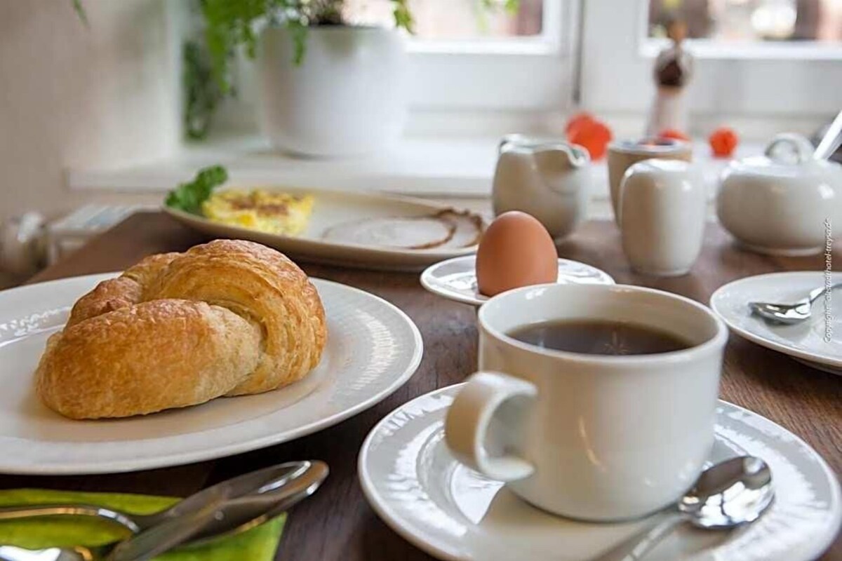 A breakfast setting with a croissant, a cup of coffee, and a plate of eggs.