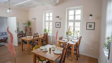 Een eetgedeelte met houten tafels en stoelen, grote ramen en plafondventilatoren.