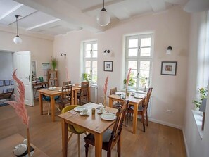 A dining area with wooden tables and chairs, large windows, and ceiling fans. - Altstadthotel Treysa (Schwalmstadt)