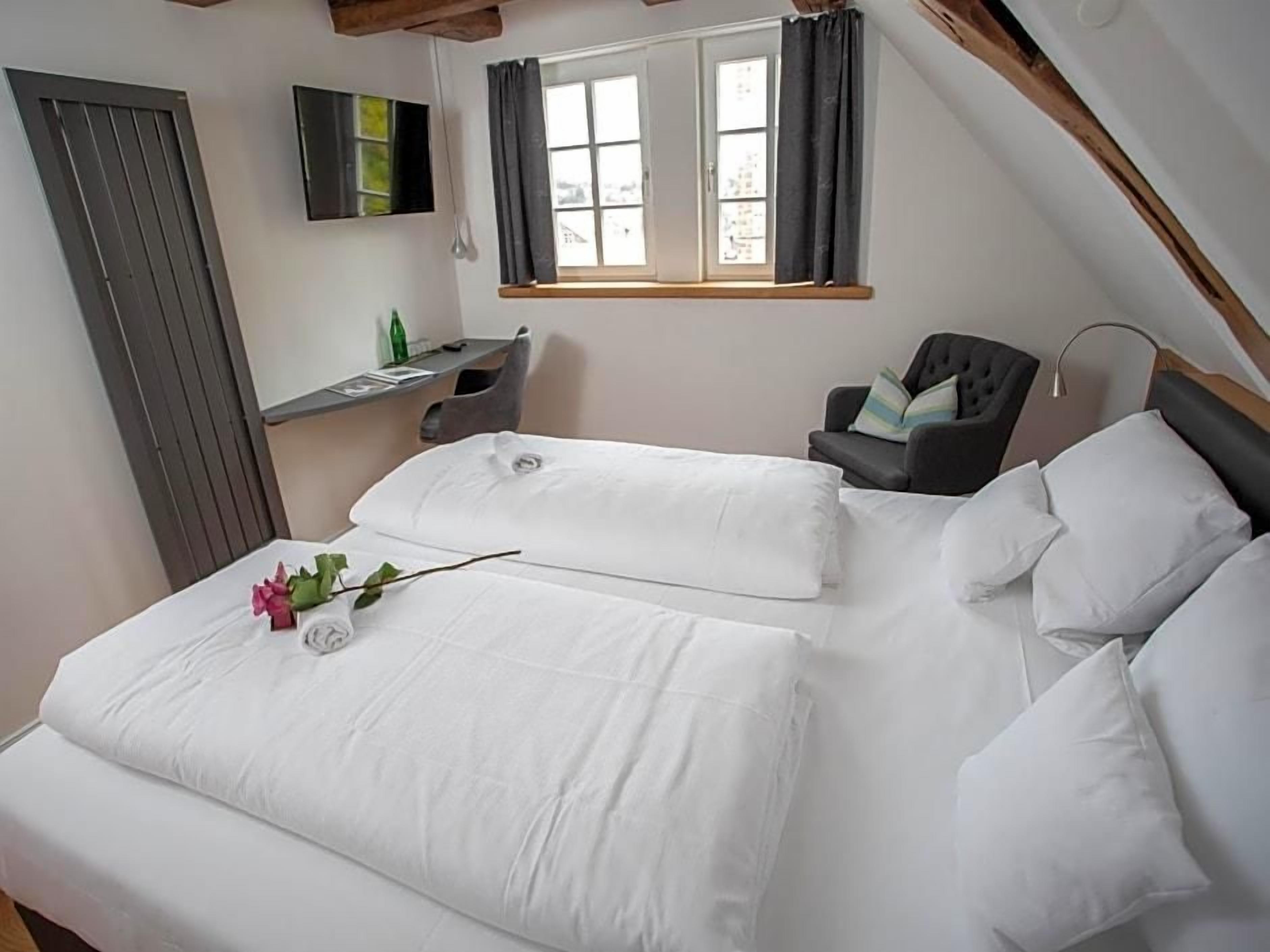 A bedroom with two beds, a desk, a chair, and a window with curtains.