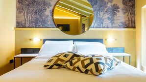 Habitación de hotel con cama, dos almohadas, espejo redondo y pared con diseño de árbol.