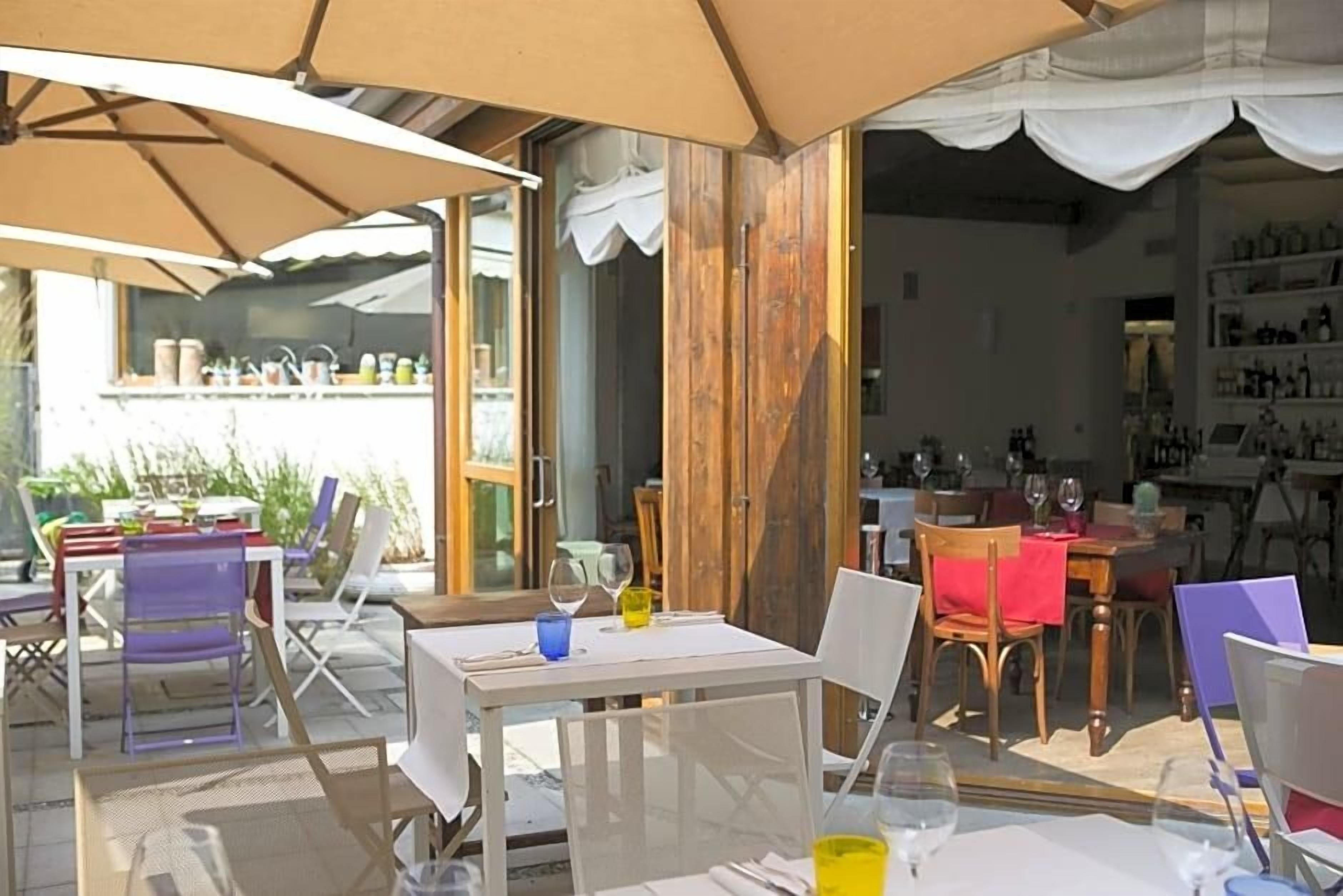 An outdoor dining area with tables and chairs, umbrellas, and a view of the interior.