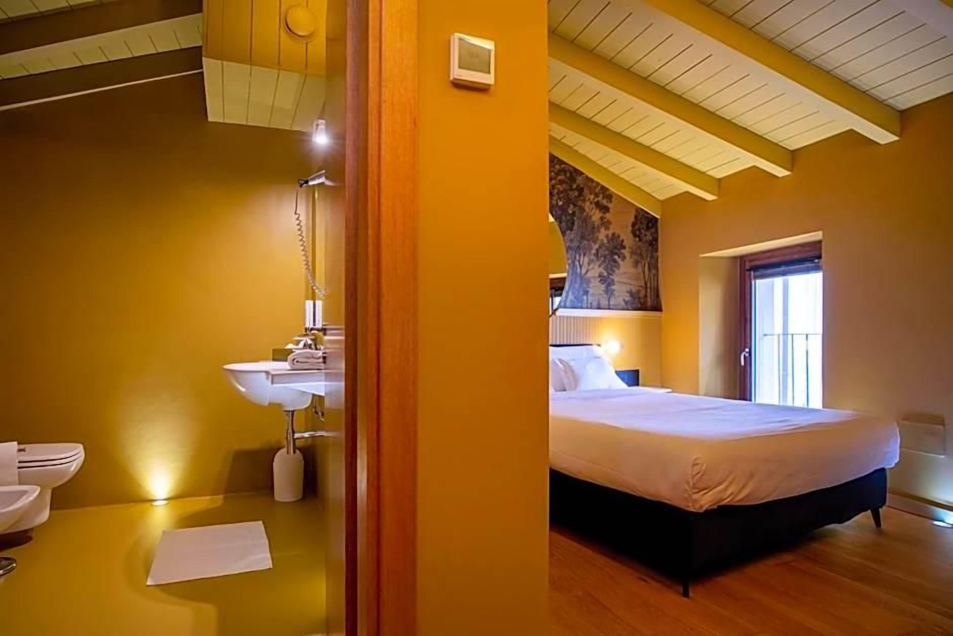Una camera da letto con un letto, un comodino, una finestra e un bagno con lavandino e water.