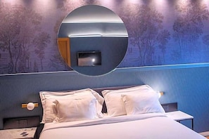 A hotel room with a large round mirror, a bed with white linens, and a wall with a tree mural. - Albergo La Braseria (Osio Sotto)