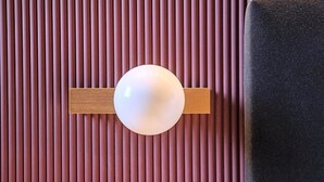 Una lámpara esférica fijada a la pared, sobre un revestimiento con líneas verticales.