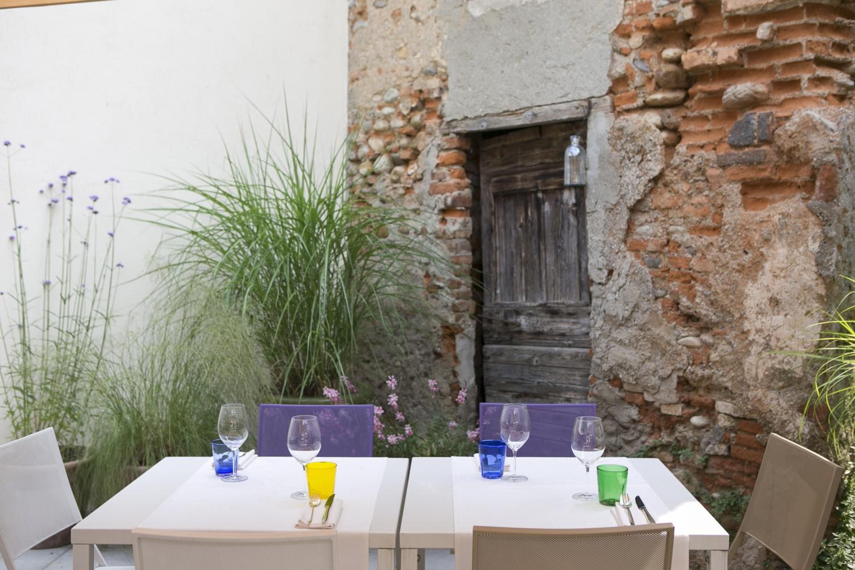 An outdoor dining area with two white tables, each set with a wine glass and a cup.