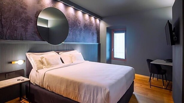 Un dormitorio moderno con una cama grande, una mesita de noche, un escritorio y un espejo en la pared.