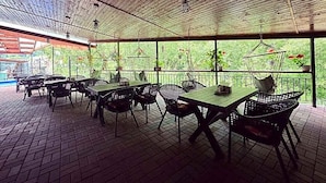 An outdoor patio area with tables and chairs, a wooden ceiling, and a view of greenery. - Maison Platanus (Voineasa)