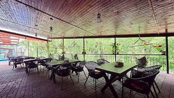 An outdoor patio area with tables and chairs, a wooden ceiling, and a view of greenery.