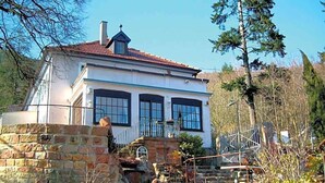 Una casa de dos pisos con un muro de piedra, una escalera metálica y cielo despejado.