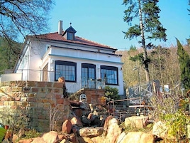 Una casa de dos pisos con un muro de piedra, una escalera metálica y cielo despejado.