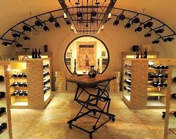 Una bodega con una mesa central, estanterías llenas de vino a cada lado y un arco circular.