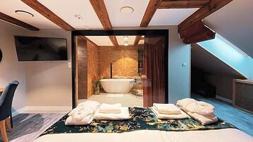 Un dormitorio moderno con una cama grande, televisor y baño con bañera y ducha.