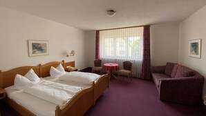 Quarto de hotel com cama, escrivaninha, cadeira, sofá e janela com cortinas.