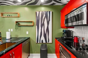 Una cocina con gabinetes rojos, encimera negra, extractor de acero inoxidable y un cuadro abstracto grande en la pared.