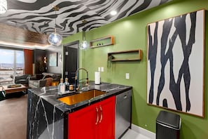 Una cocina moderna con encimera de mármol negro, armarios rojos y un cuadro con estampado de cebra.