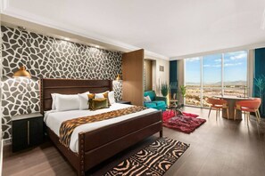 Una habitación de hotel moderna con una cama grande, vistas al desierto y un área de descanso con dos sillas.